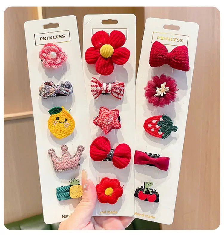 A hand holds a pack of five adorable flower-shaped baby hair clips in various colors and textures.
