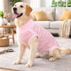 Ein golden Retriever mit einem rosa-weiß gestreiften West über einem hellgrauen Teppich drinnen.