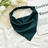A dark teal triangle scarf is draped on a white linen cloth next to a piece of paper.