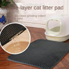 Un tapis à litière noir à double couche à côté d'une boîte à litière pour animaux blanche et d'un plancher en bois.
