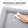 A hand wipes liquid beads off a gray pet mat, demonstrating its waterproof and urine-proof features.
