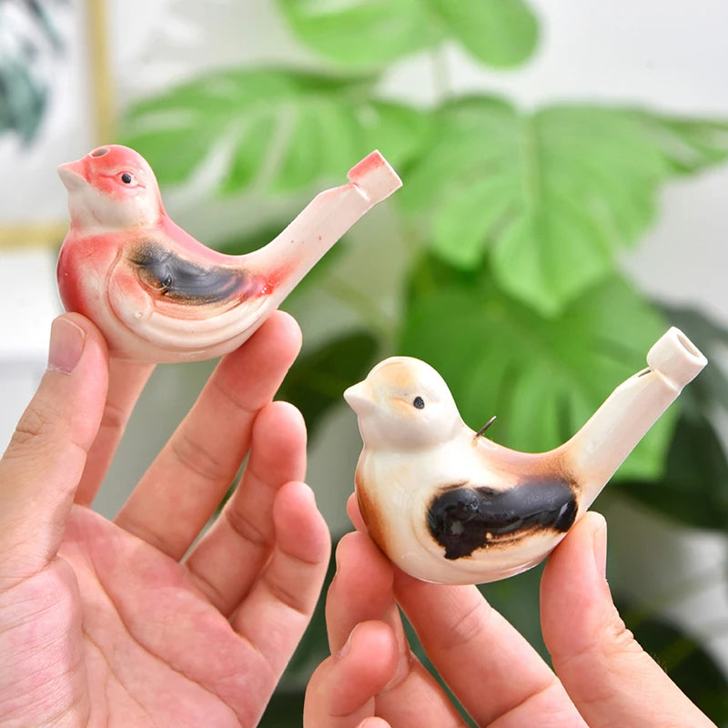 Eine Hand hält eine rosa und schwarze Wasservogel-Pfeife für Kinder vor einem unscharfen grünen Blätterhintergrund.