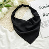 Black fabric triangle head scarf draped on a white surface next to white flowers and a book.