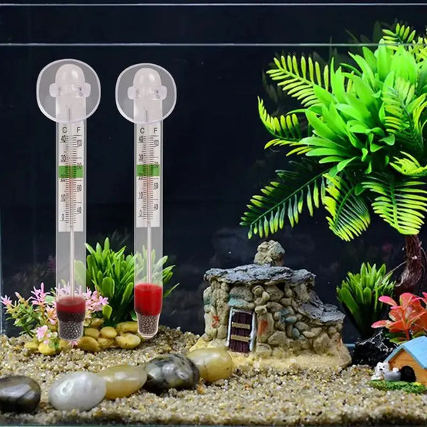 A vertical floating aquarium thermometer with a glass tube and scale is displayed in a miniature landscape.