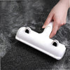 A hand is using a white reusable pet hair remover brush with suction on a dark surface.