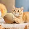 An orange kitten plays with a woven sisal scratching ball on a light-colored surface.