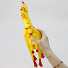 A hand is holding a bright yellow squeaky rubber chicken dog toy with orange accents against a light gray background.
