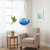 A light beige armchair sits next to a window with sheer white curtains, featuring a blue and white bird hanging hammock.