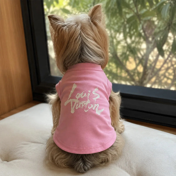 A light brown dog is lying down, looking over its back at a pink pet singlet with white text that reads Louis Burton.