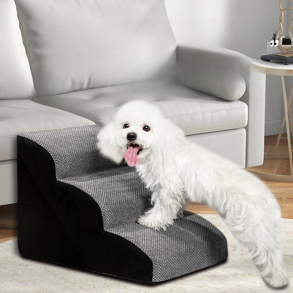A fluffy white dog is standing on a black and gray pet ramp in front of a light gray sofa.