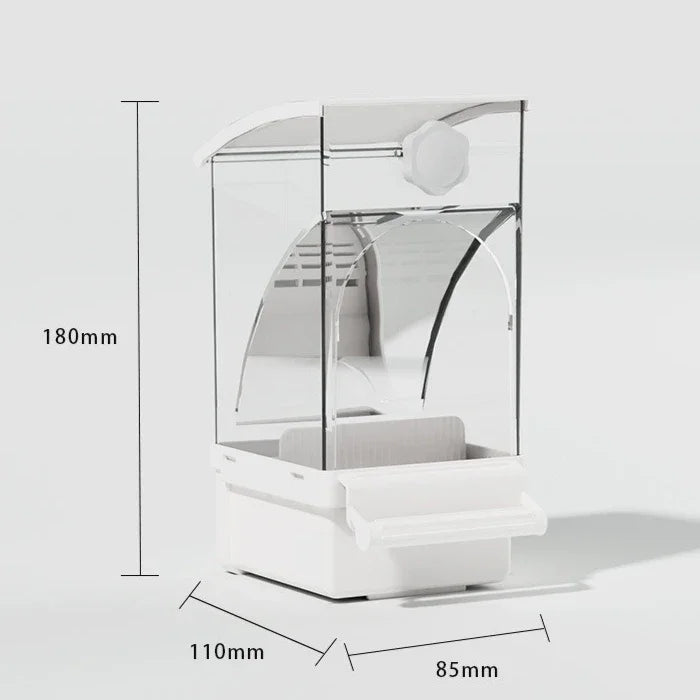 A clear plastic automatic parrot feeder with a white base and feeding tray, shown from the side.