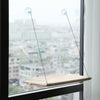 A beige hanging cat hammock suspended by thin wires from suction cups in a window.