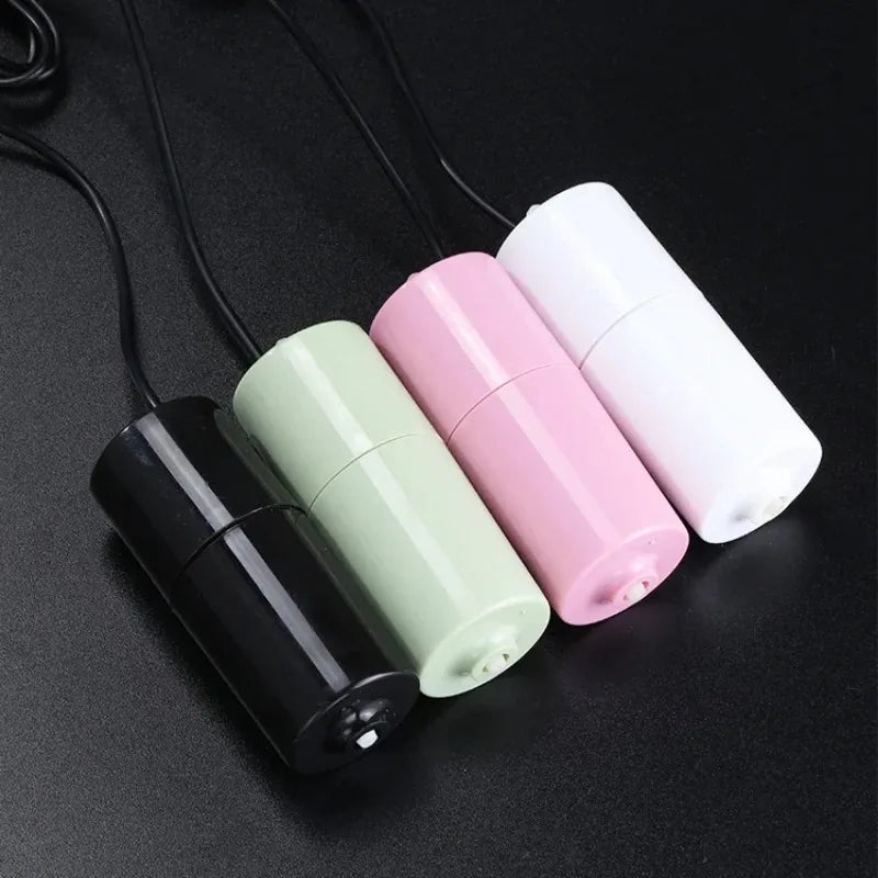 Three portable USB aquarium air pumps in black, light green, and pink lying on a dark surface.