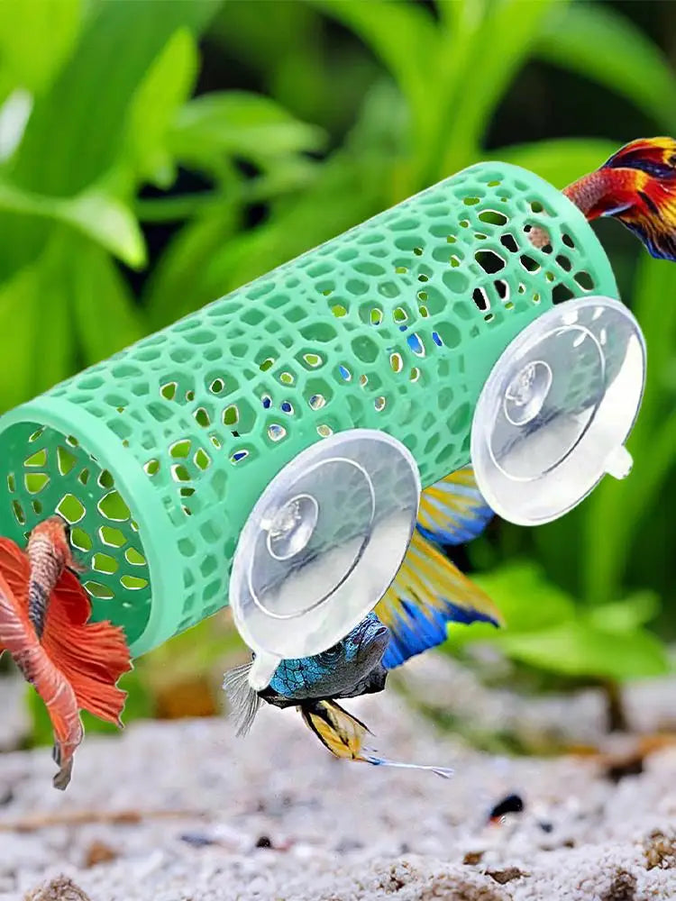 A green aquarium hideout tube with suction cups is shown in a natural, leafy outdoor setting.