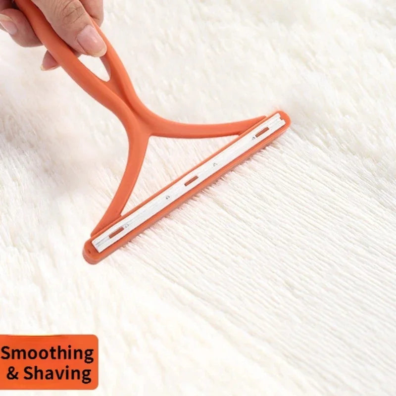 An orange 2-in-1 pet hair remover and fabric shaver is being held over a white, fluffy surface.