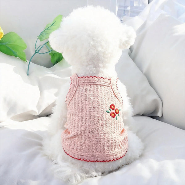 A fluffy white dog wearing a pink knitted summer thin strap pet collar lying on white bedding.