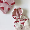 Sudadera blanca con estampados de corazón rojo y forro rosa, doblada sobre una superficie blanca.