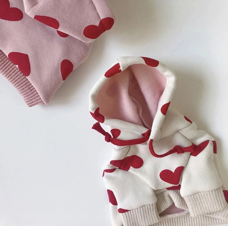 Sudadera blanca con estampados de corazón rojo y forro rosa, doblada sobre una superficie blanca.