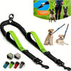 A black dual dog leash coupler with green padded handles and shock-absorbing bungee attached to a leash.
