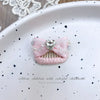 Pink bow hair accessory with rhinestone and pearl accents displayed on a white plate.