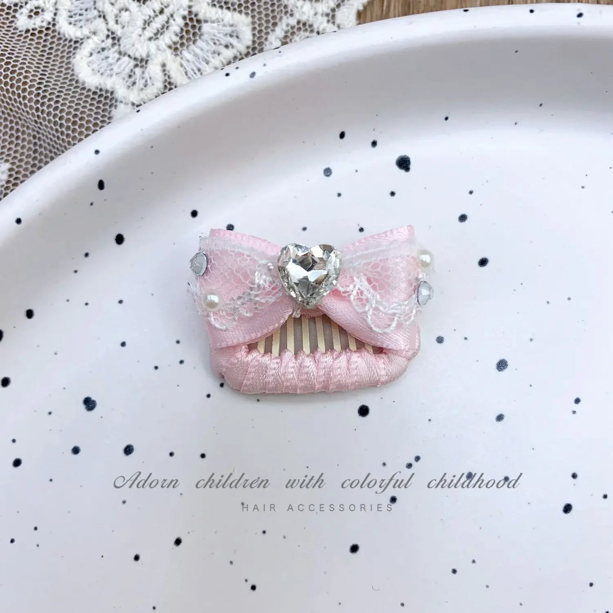 Pink bow hair accessory with rhinestone and pearl accents displayed on a white plate.