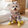 A small white dog wearing a cartoon printed raincoat with yellow paws sitting on a light surface.