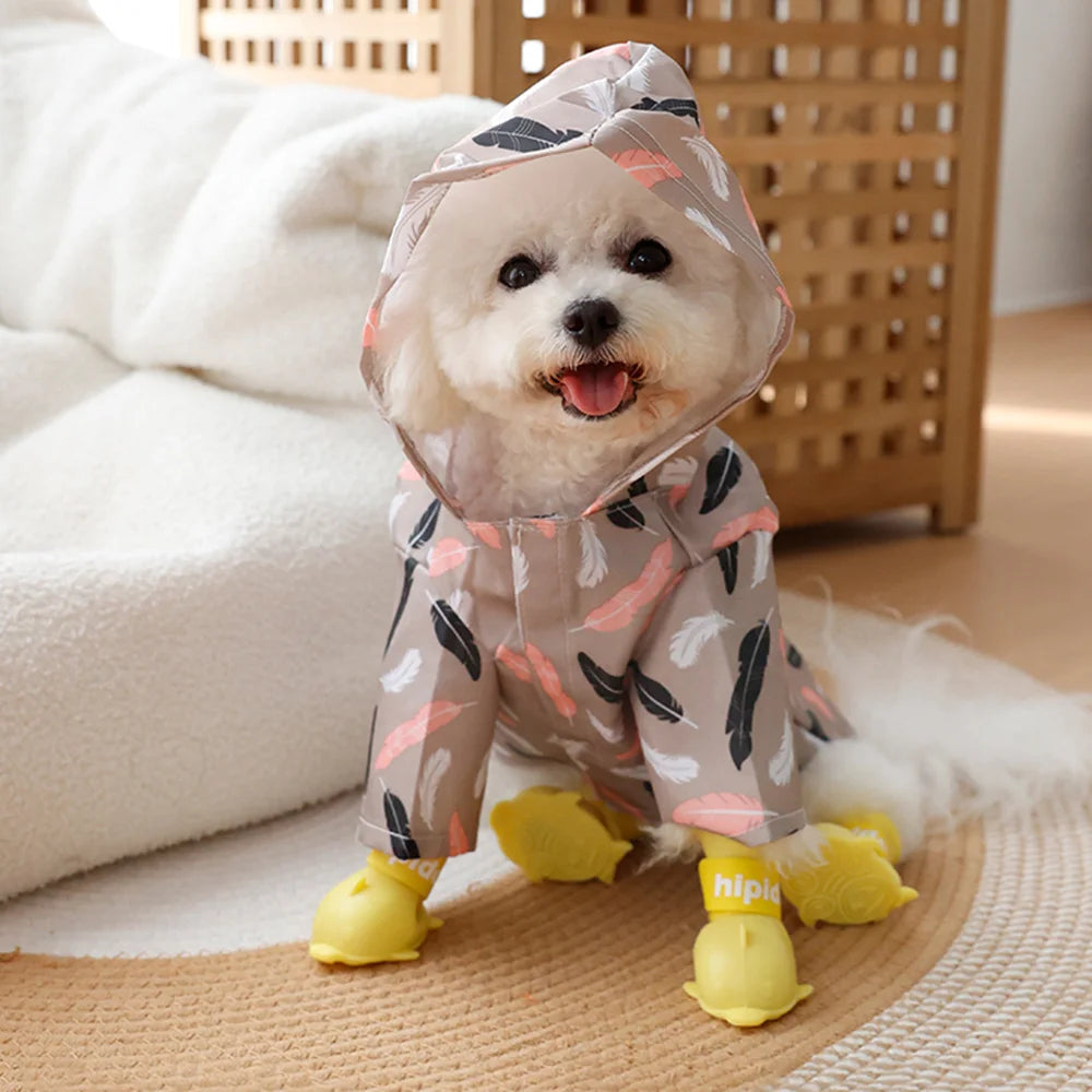 A small white dog wearing a cartoon printed raincoat with yellow paws sitting on a light surface.
