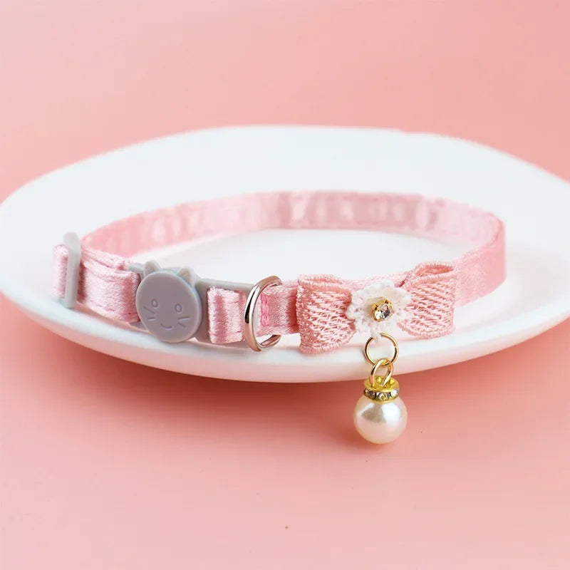 Pinkes Spitzenhalsband für Haustiere mit runder Anhänger, Hängemal, und kleinen Klingel auf weißem Teller.