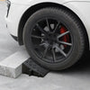 A close-up view of a black wheel with a red brake caliper mounted on a white car tire resting on a gray concrete ramp.