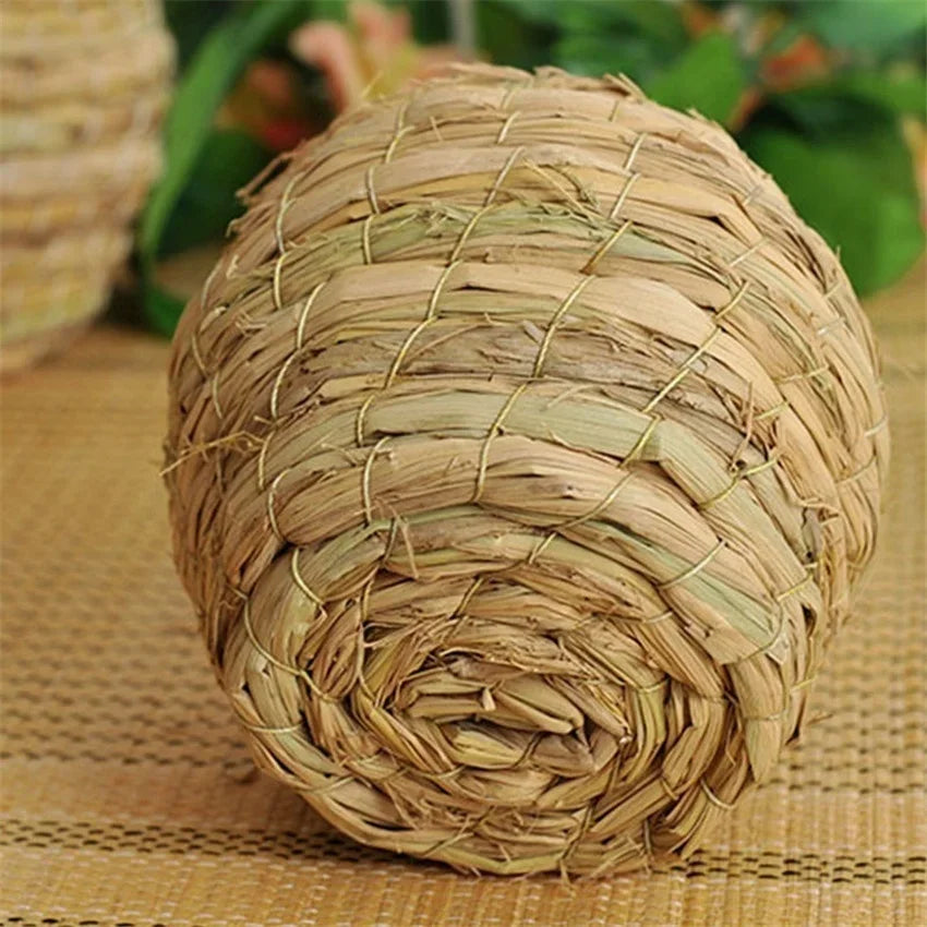 A tightly woven natural straw bird nest for pet avians resting on a woven mat.