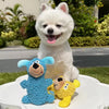 A white fluffy dog sits next to two blue and yellow plush toys on a white surface.
