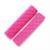 Two pink quilted plush car seat belt shoulder protectors lying diagonally on a white background.