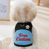 Un perro blanco y esponjoso vistiendo un arnés de mascota negro y azul con el texto Free Custom en la parte delantera.