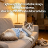A fluffy gray and white cat wearing a light blue breathable vest is relaxing on a sofa.