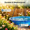 A blue glass bird bath fountain hanging by chains outdoors with colorful flowers in the background.