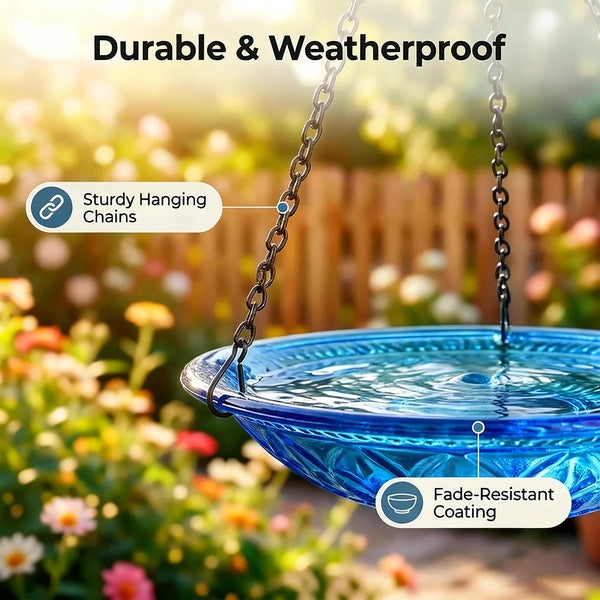 A blue glass bird bath fountain hanging by chains outdoors with colorful flowers in the background.
