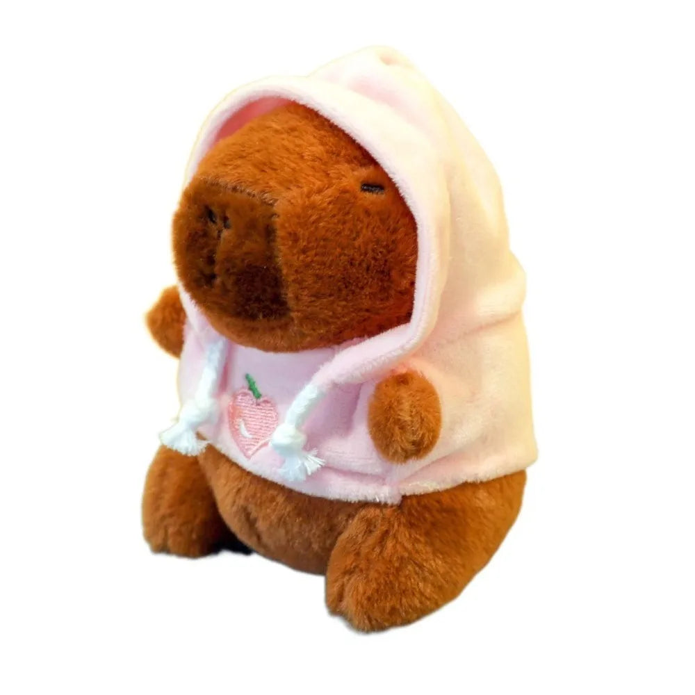 A brown capybara plush doll wearing a pink hoodie with white trim.