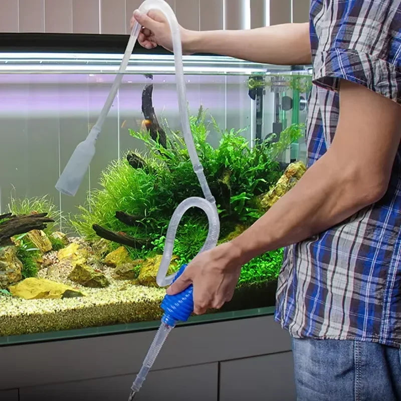 A person uses an aquarium gravel cleaner and water changer with a siphon pump to clean fish tank substrate.