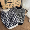 A black and white knit sweater for dogs with a repeating monogram pattern resting on a brown surface.