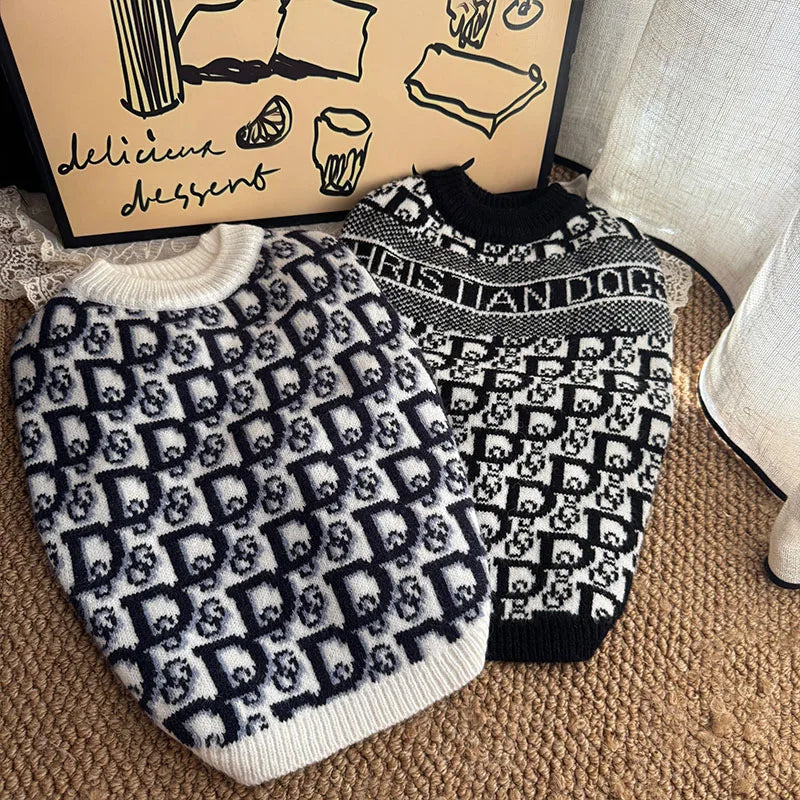 A black and white knit sweater for dogs with a repeating monogram pattern resting on a brown surface.