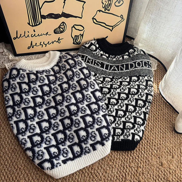 A black and white knit sweater for dogs with a repeating monogram pattern resting on a brown surface.