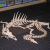 A white articulated dragon skeleton model displayed on a dark cutting mat.