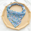 A light blue floral triangle head scarf is displayed on a round beige plate.