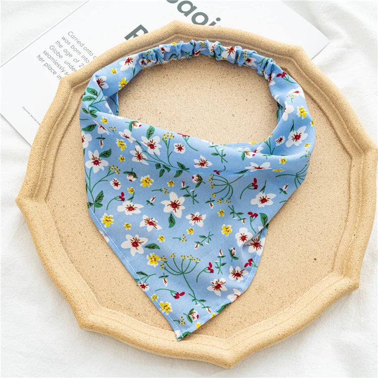 A light blue floral triangle head scarf is displayed on a round beige plate.