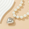 A delicate pearl choker necklace featuring a heart-shaped silver pendant, displayed against a light beige background.
