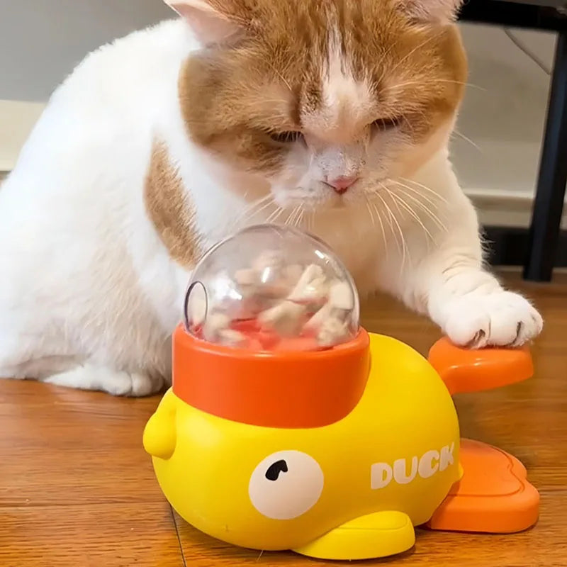 Eine Katze schaut auf einen gelben, duckförmigen Puzzle-Spielzeugspender für Leckerlis.