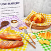 A variety of baked goods including bread rolls and scones are displayed on a white surface with yellow and green checkered pa