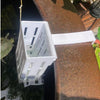 A white wall-mounted hydroponic plant basket is suspended over water, likely for an aquarium or pond.