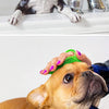 A brown dog is being groomed with a green rubber pet grooming brush by a person.