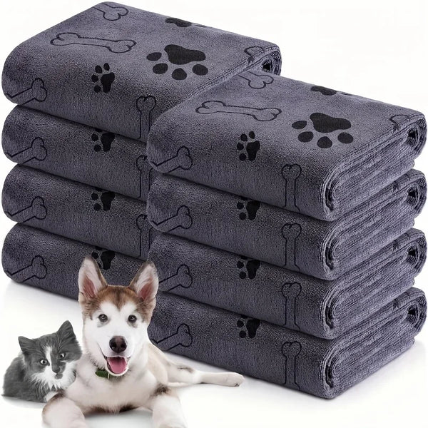 A stack of gray microfiber pet bath towels with paw print designs next to a dog.